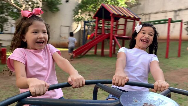 2 fun little girl playing at playground roundabout carousel in motion