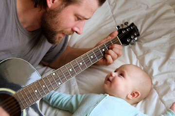 Bearded Father Playing Guitar to his Little Child. Baby Looking at Him, Listening and Smiling....