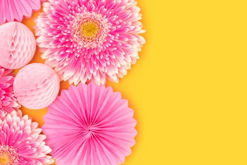 Tuinposter Pink gerbera flowers, tissue paper fans and balls on a yellow background. Place for your design. © rorygezfresh