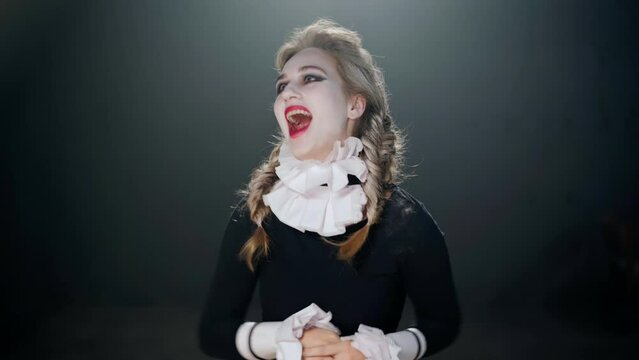 Medium shot portrait of young Caucasian actress in costume imitating insanity laughing out loud looking at camera. Talented female performer posing on stage in theater playing madness role