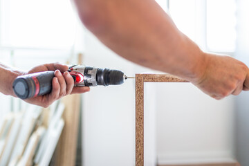 Man hands holding electrical screwdriver while assembling kitchen wooden elements.