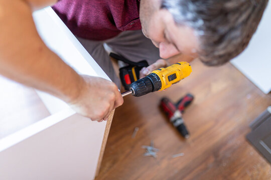Close up of man holding electrical battery screwdriver while installing wooden kitchen shelves