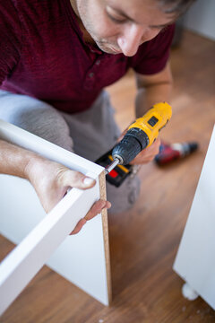 Man installing wooden shelves by using cordless screwdriver