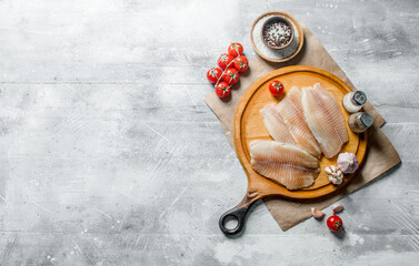 Fish fillet on a round cutting Board with spices, tomatoes and garlic.