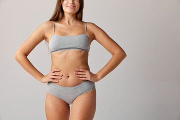 Cropped image of slim female body, breast, belly and buttocks in cotton underwear over grey studio background. Concept of body and skin care, fitness