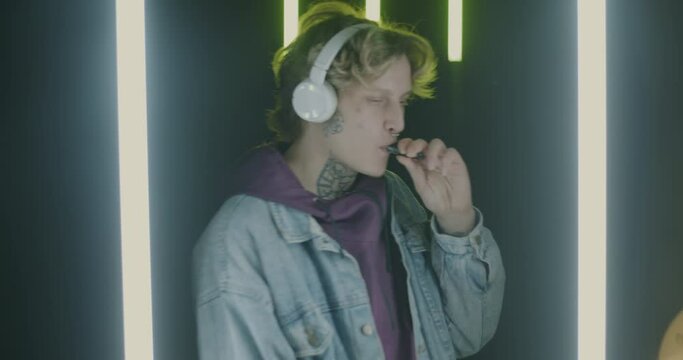 Slow motion portrait of young man wearing headphones enjoying music and vaping dancing in futuristic neon light. People and smoking concept.