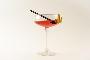 Champagne coupe with pink lady cocktail, lemon twist and black straw isolated on a white background