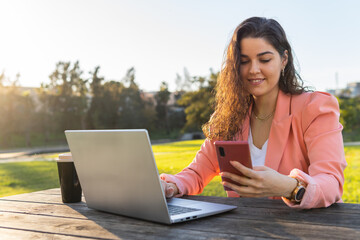 Businesswoman with her laptop while checking her cell phone.
