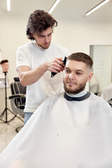 Obraz premium Barber trim hair with clipper on handsome bearded man
