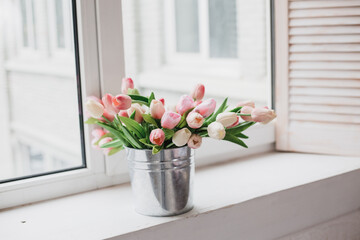 
Spring flowers in vase on breakfast tray. White tulips in a vase in a rustic interior. Cozy apartment in boho chic style interior