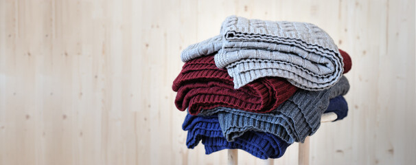Stack of warm, multicolored pullover knitwear, collection of handmade wool sweaters on stool against light wooden background