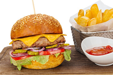 Juicy appetizing hamburger with fried beef cutlet, slices of cheddar cheese, tomatoes, green vegetables and basket of fried potatoes with ketchup on wooden board