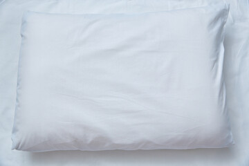 Top view of a white pillow against a white sheet. Copy space.