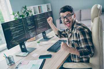 Photo of excited lucky coder dressed eyewear rising fists web designing modern gadget indoors...