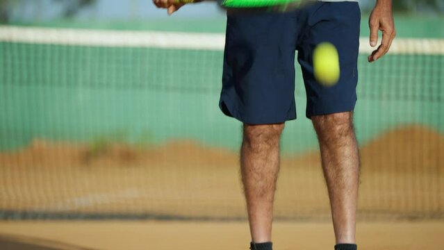 tilt up shot of Healthy active senior man practising tennis by tapping ball on groud at court - concept of practising, healthy lifestyles and morning routine.