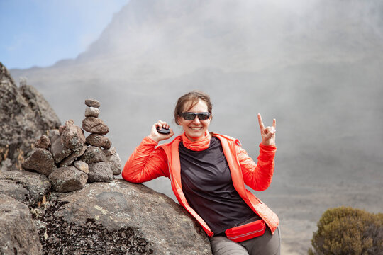 Happy Hiking Woman In Orange Jacket Against The Background Of Big Cloud In Mountains.