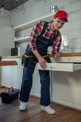 Joyous repair technician repairing a piece of kitchen furniture