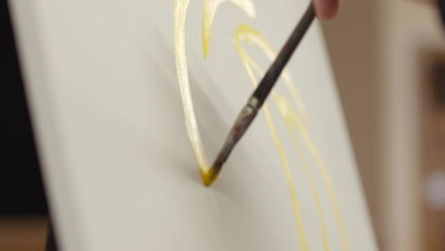A male artist in a large hall holds a brush in his hand and draws a yellow line on canvas. The artist paints on canvas.