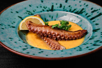 Cream soup with octopus on blue plate on black background