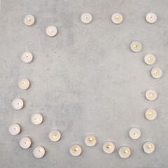Tea light candles on stone background with copy space. Burning small candles  on cement surface, top view.