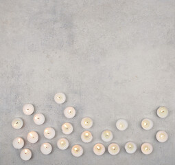 Tea light candles on stone background with copy space. Burning small candles  on cement surface, top view.