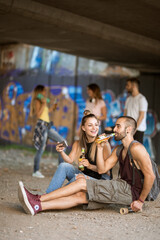 Young man siting on a skateboard and drinking with friends