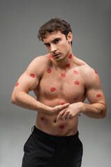 Naklejka premium athletic man with red lip prints on shirtless muscular body looking at camera on grey background.