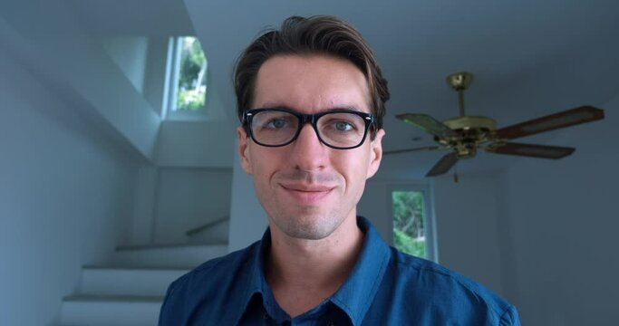 Portrait of a young man, 30 years old, in a blue shirt, puts on glasses to see better and smiling against the backdrop of an indoor home office. Correction of vision with glasses