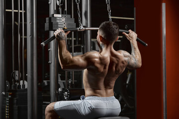 Fototapeta na wymiar Portrait of young muscular man training shirtless in gym indoors. Doing lat pull down exercises. Side view. Relief, muscular back. Concept of sport, workout, strength