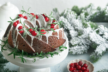 Christmas chocolate bundt cake. Traditional Christmas fruit cake with white glaze, cranberries and rosemary on white stand with Christmas decoration. Winter baking at Xmas or New Year. Copy space.