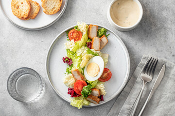 Caesar salad in modern linear feed. Healthy salad made with chicken, egg, cherry tomatoes, iceberg lettuce and parmesan chips with cutlery on gray table. Light diet dinner, text space, menu