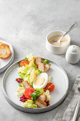 Caesar salad in modern linear feed. Healthy salad made with chicken, egg, cherry tomatoes, iceberg lettuce and parmesan chips with cutlery on gray table. Light diet dinner, text space, menu