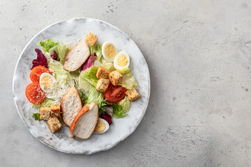Caesar salad. Healthy salad made with chicken fillet, cherry tomatoes, iceberg lettuce, parmesan cheese and croutons on light grey background top view with copy space. Light diet dinner, text space