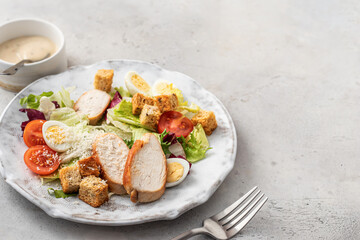 Caesar salad. Healthy salad made with chicken fillet, cherry tomatoes, iceberg lettuce, parmesan cheese and croutons on light grey background with cutlery. Light diet dinner, space for text