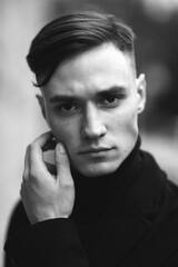 Fashion portrait of a young guy in black clothes of model appearance on the street among skyscrapers and alleys