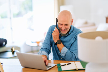 Middle aged businessman using laptop and mobile phone for work at home