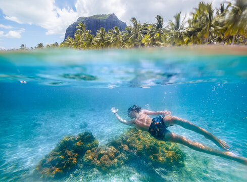 Diving teenage boy snorkeling over the coral reefs underwater photo in the clean turquoise lagoon on Le Morne palm trees beach with Le Morne Brabant mount. Mauritius island. Exotic traveling concept.