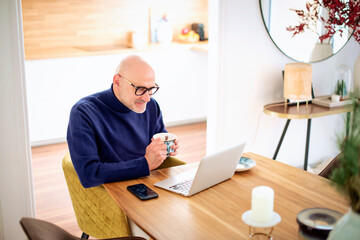 Middle aged businessman wearing casual clothes and using laptop while working from home