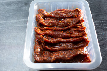 A view of spicy marinated beef, in a plastic container.