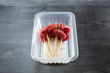 A view of a plastic container of pickled pepper beef on skewers.