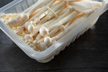 A closeup view of a plastic container of large enoki mushrooms.
