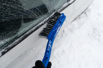 Removing snow from the car on a cold winter day. Snow removal after snowstorm. Snow cleaning and...