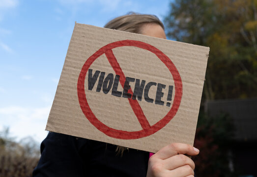 Woman holding a cardboard banner sign with word Violence strikethrough. Female protester with Stop Violence placard at protest rally demonstration.