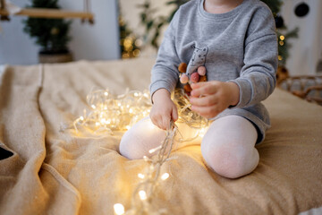 The child is playing with a light garland, a Christmas tree decoration.