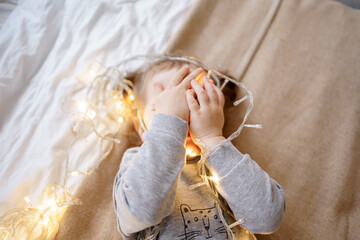 The child is playing with a light garland, a Christmas tree decoration.