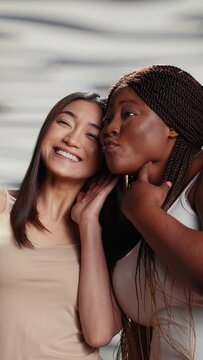 Vertical video: Two skincare models taking pictures on smartphone, using mobile phone to have fun with photos. Young beautiful women promoting self love and body positivity, self acceptance in studio.