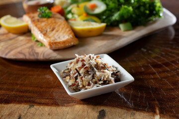 A view of a salmon filet entree, featuring a side dish of wild rice mix.