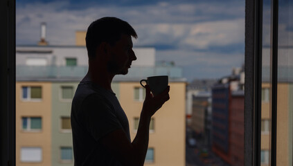 silhouette of a man with a mug of tea on the background of the city.