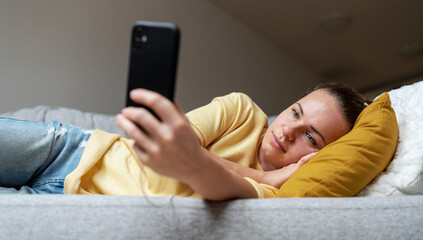 Woman with blank expression face lying on sofa and using her cell phone.