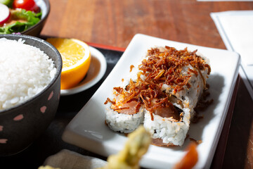A view of a yellow tail sushi roll, topped with fried onions.